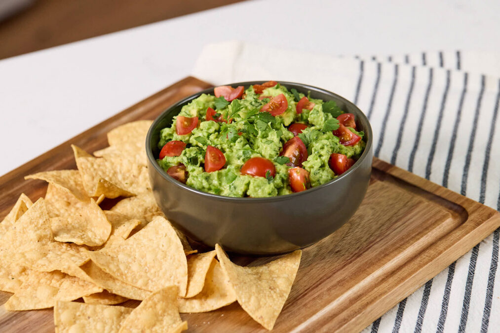 Bowl of chunky California avocado guacamole on a cutting board with tortilla chips