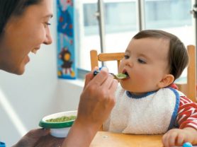 Mother feeding baby mashed avocado