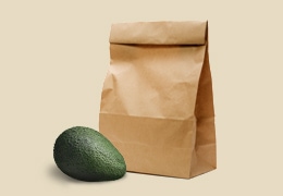 A whole avocado next to a paper lunch bag