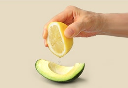 Lemon being squeezed onto an avocado slice
