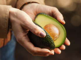 Close up of hands holding a California avocado sliced in half